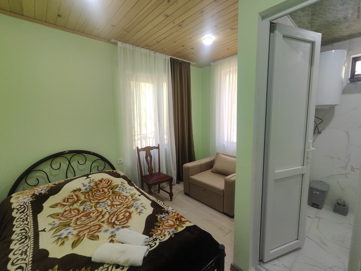 A green guest room with a double bed and the door to its private bathroom open.