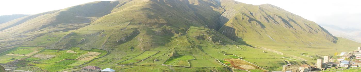 A wide view of the country around Ushguli: bare ridges, green pasture and the road running along the valley floor.